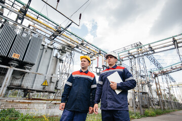 Two specialist electrical substation engineers inspect modern high-voltage equipment. Energy....
