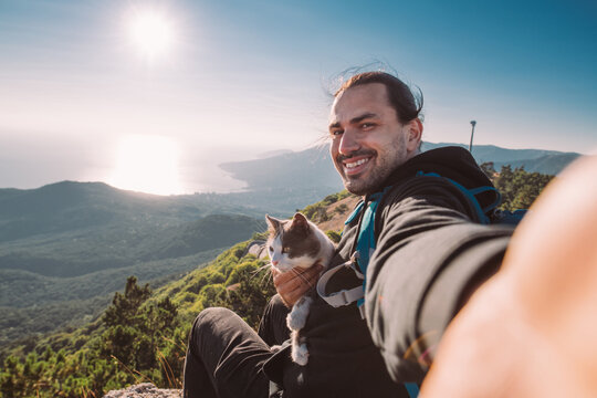 A man tourist with a cat makes a selfie in the mountains at dawn