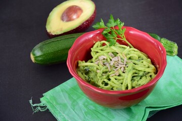 Fresh organic raw zucchini noodles or zoodles with avocado pesto sauce garnish with parsley and sunflower seeds. 