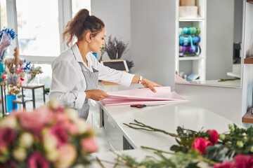 Enthusiastic brunette woman touching gift-wrapping paper on the table