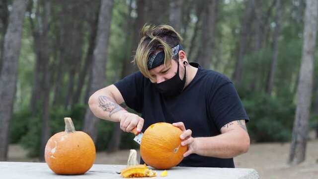 Hombre joven con tatuajes vaciando una calabaza de halloween
