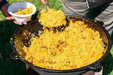 Big cauldron with tasty pilaw just cooked outdoors on picnic on sunny day.