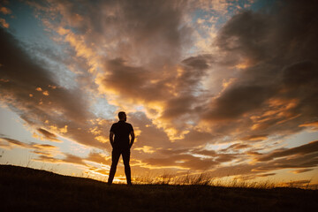 Back view of a young man stands on a mountain at sunset. A view of the beautiful sky at sunset in the nature 