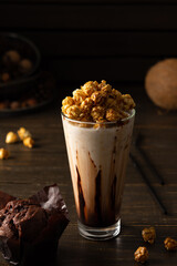 Tall glass cup with chocolate milkshake and caramel popcorn and chocolate muffin on wooden background