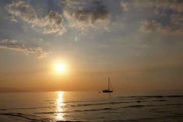 Naklejka na ściany i meble A single sailboat near the sun on the horizon with a brilliant orange sky