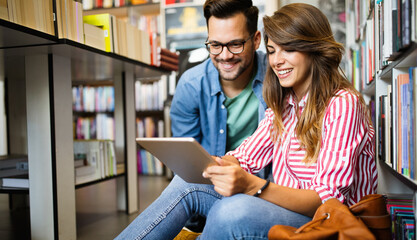 Group of happy students reading books and preparing to exam in library