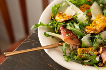 Light autumn salad with arugula, baked pumpkin, prosciutto and young parmesan, a plate of salad on a wooden table