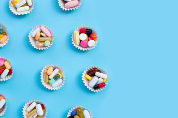 Colorful tablets with capsules and pills in cupcake wrappers on blue background.