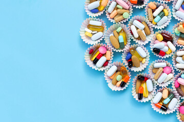 Colorful tablets with capsules and pills in cupcake wrappers on blue background.