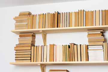 Light wooden bookshelves with hardback overturned books in white interior, home library