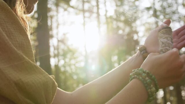 occult science and supernatural concept - young woman or witch with smoking white sage performing magic ritual in forest