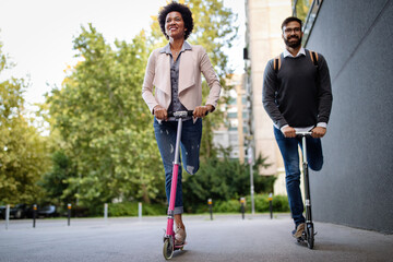 Two smiling business people driving electric scooter going to work.