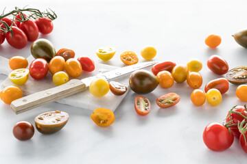 Assorted cherry tomatoes with a knife and cutting board against a white background. 