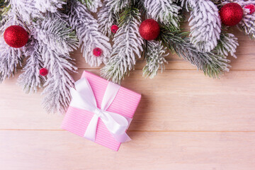 Pink gift box, Christmas decoration and frosty fir tree branches over wooden background with copy space