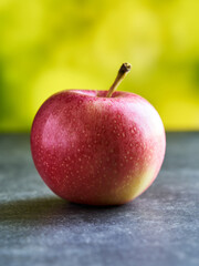 Red apple lies on gray texture, green background is nicely blurred