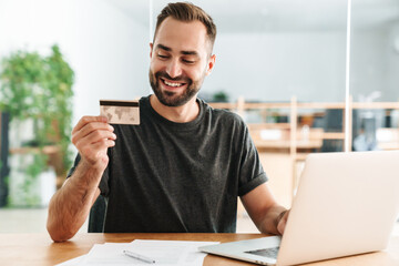 Happy man smiling and holding credit card while working with laptop