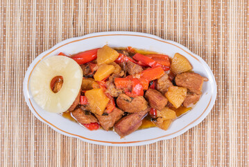 Adobe pork with pineapples and bell peppers in an oval plate on a bamboo napkin, top view - philippine cuisine