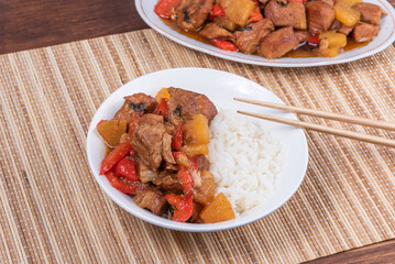 Adobe pork with pineapple and bell pepper in an oval plate and a bowl of rice with chopsticks on a bamboo napkin - philippine cuisine