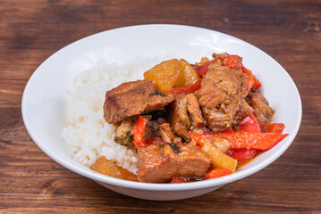 Adobo pork with pineapple and pepper in bowl with boiled rice on wooden dark background