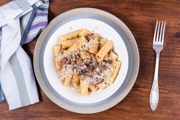 Pasta alla gricha with pancetta in a plate on a dark wooden table close up, top view