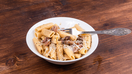 Pasta alla gricha with pancetta in a plate on a dark wooden table close up, top view