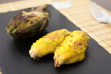 cooked fried chicken wings and halves artichokes on black stone plate