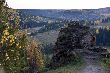 Obraz premium A gray stone rock on a steep wooded slope of a deep river valley. In the foothills of the Western Urals, golden autumn.