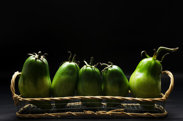 Closeup of basket full of green fresh and juicy tomatoes against black background.Empty space
