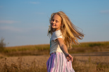 Obraz premium Beautiful little girl with a bouquet of wild flowers on a background of the sky. A happy child on a summer meadow.