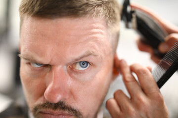 Obraz premium Portrait of a pensive man who is being cut with a machine. Haircut at home concept