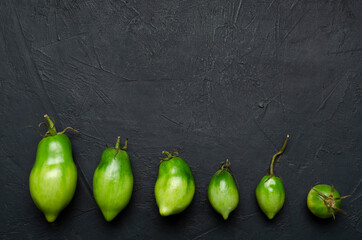 Top view of different shapes and sizes of green juicy tomatoes on the dark surface.Process of growing.Empty space
