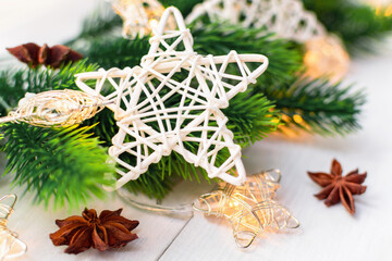 Christmas wicker star, festive decorations with Christmas tree and garland lights on a white wooden background, close-up.