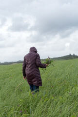 Woman in purple coat holding fresh wild flower bouquet while walking on sand dune covered in grasses on Oregon Coast