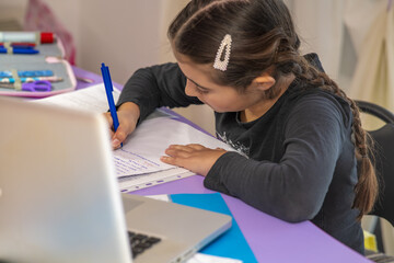 Young schoolgirl studying homework during her online lesson at home, social distance during quarantine, self-isolation, online education concept, home schooler