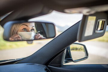 Young woman driving car with protective mask on her face.