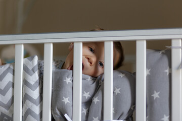 Cute european baby boy is chewing a cot side. Image with selective focus.