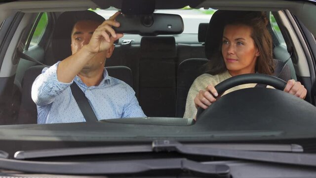 driver courses and people concept - woman and driving school instructor adjusting mirror in car