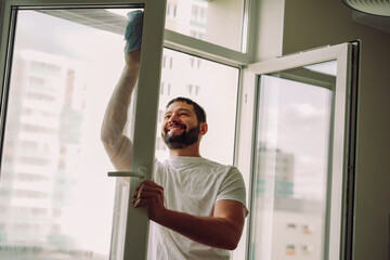 Young handsome bearded man doing spring cleaning in an apartment. washing window with cloth