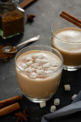 Hot chocolate with whipped cream in glass isolated with cinnamon stick, over dark background