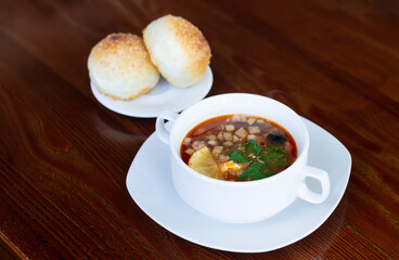Bowl of meat vegetable soup next to bread buns
