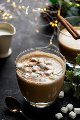 Coffee cup with milk foam and marshmellows, Christmas lights and decorations background. Copy space.