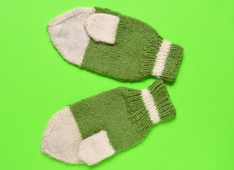 handmade white and green winter baby mittens. green background. winter, christmas and new year concept,