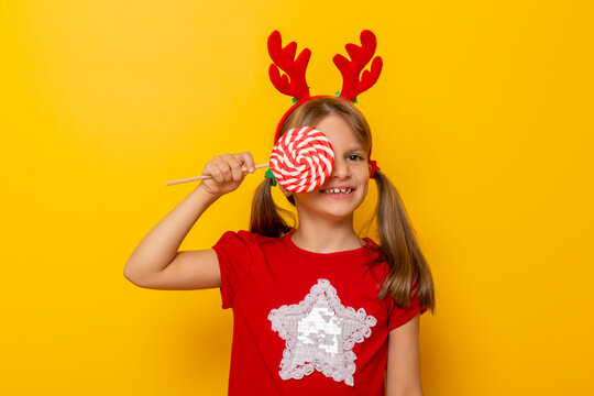 Little girl wearing antlers hiding behind big lollipop
