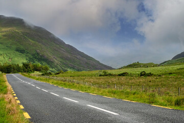 Narrow empty asphalt road into mountains, Low cloudy sky over peaks. Nobody, Connemara, Ireland. Concept travel, road trip