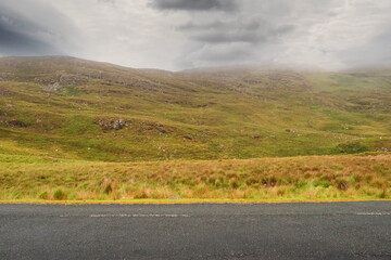 Small narrow asphalt road in Connemara and view on the mountains area. County Galway, Ireland, Low cloudy sky. Nobody