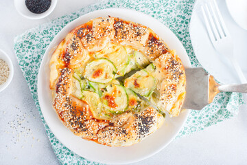 Open puff pastry zucchini pie sprinkled with poppy seeds and sesame seeds with a cut piece, selective focus