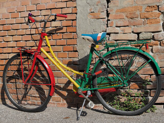 Old bicycle parked on the sidewalk, in front of a brick wall. The bike was poorly painted in many...