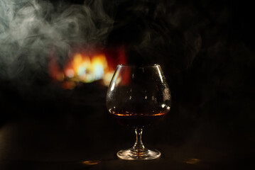 A glass of brandy and cigar smoke in the dark on the background of the fireplace. Gentlemen's club concept