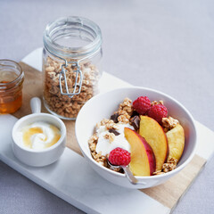 Bowl of homemade granola with yogurt, honey, fresh raspberries and nectarines on a kitchen table. Stay home Healthy breakfast. Selective focus, copy space.