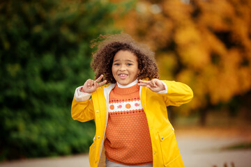 Cute afro girl smiling broadly outdoors and enjoying autumn day in park.